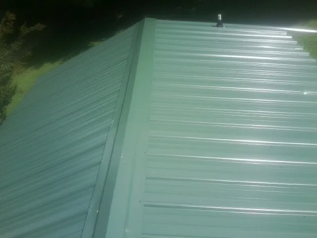 New green metal panels meeting at the ridge of a roof — Flat Roof Repair work by our crew in Hardwick
