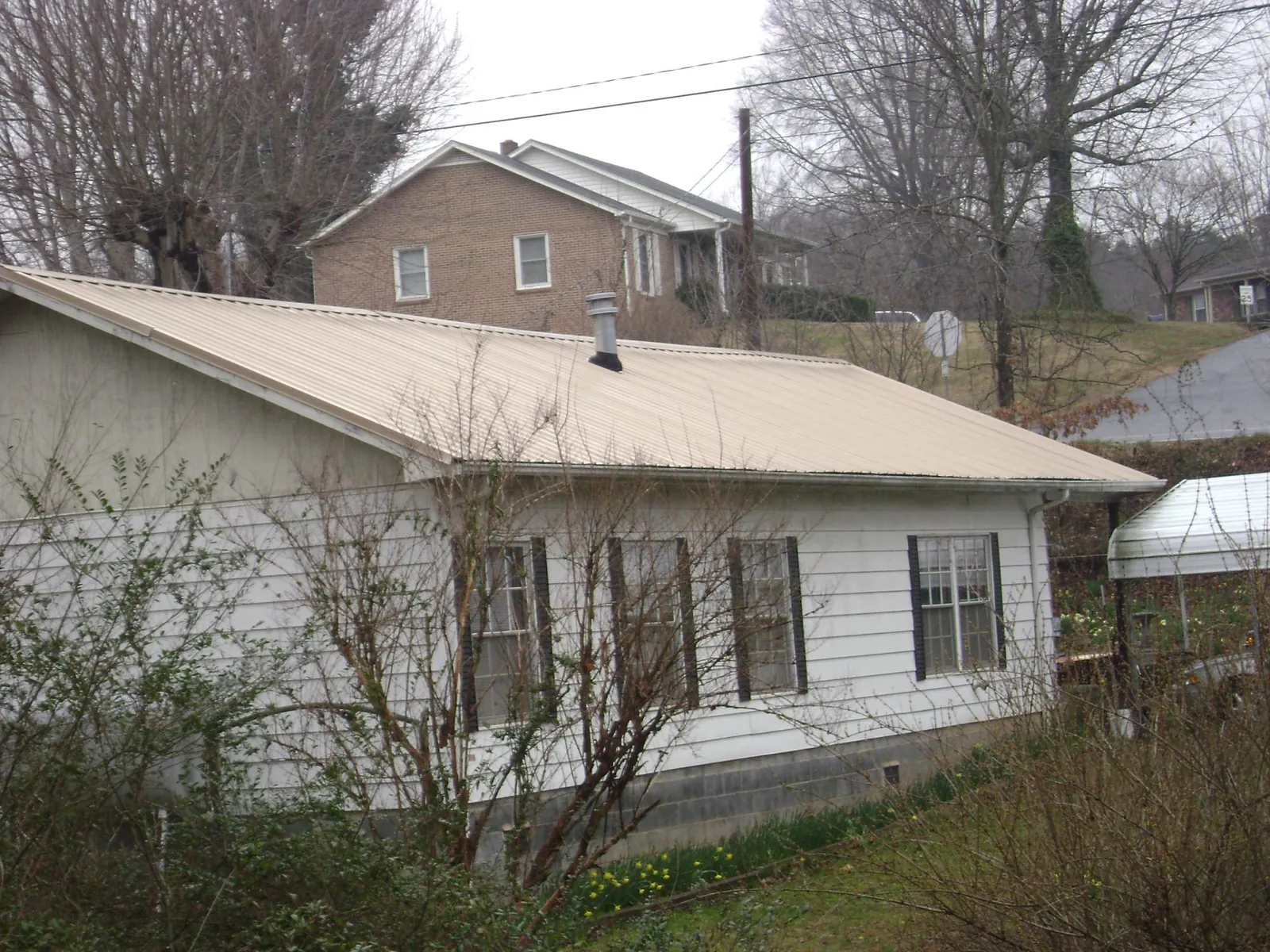 Tan metal roof on a white sided house set into a hillside — Commercial Roofing by Roofing Brothers in Hardwick